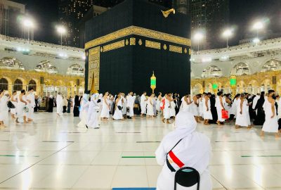 Muslim pilgrims perform Tawaf around the Kaaba in Mecca under bright lights at night.
