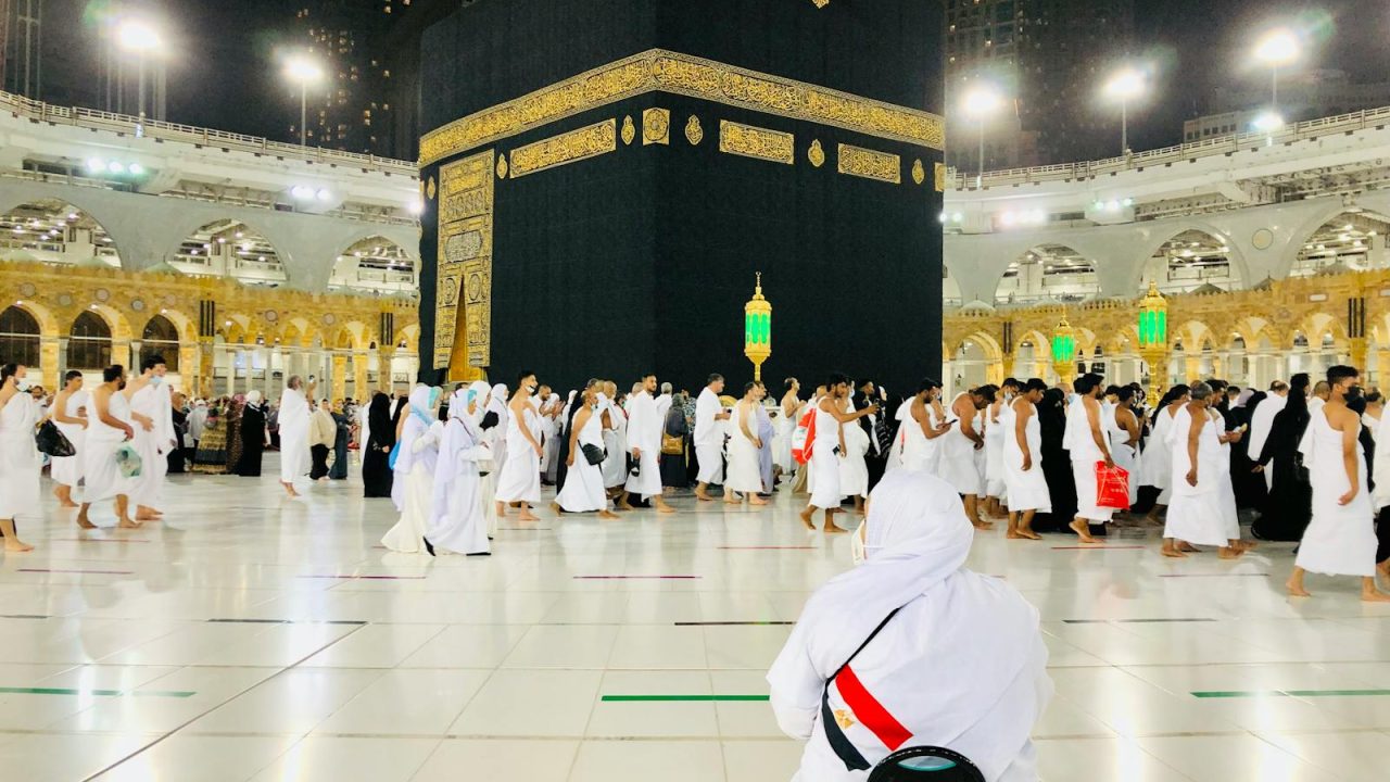 Muslim pilgrims perform Tawaf around the Kaaba in Mecca under bright lights at night.
